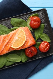 Photo of Tasty grilled salmon with tomatoes, spinach and lemon on light blue table, top view