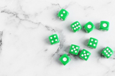 Many green game dices on white marble table, flat lay. Space for text