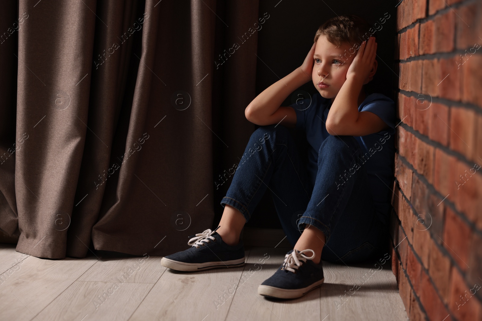 Photo of Child abuse. Upset boy sitting on floor near brick wall indoors, space for text