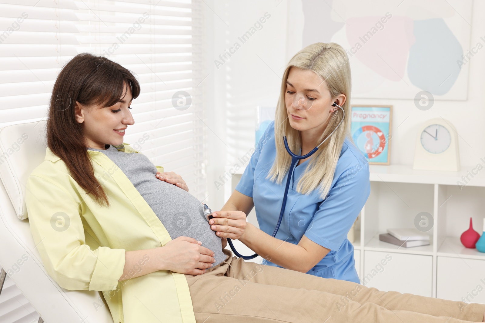 Photo of Pregnancy checkup. Doctor with stethoscope listening baby's heartbeat in patient's tummy in clinic