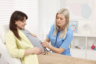 Pregnancy checkup. Doctor with stethoscope listening baby's heartbeat in patient's tummy in clinic