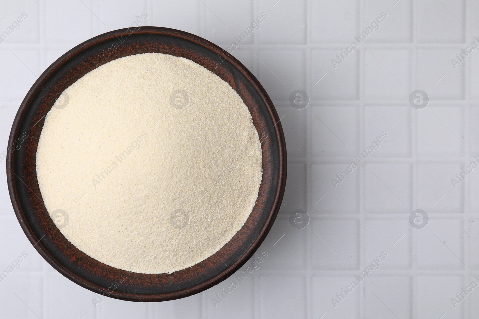 Photo of Uncooked organic semolina in bowl on white tiled table, top view. Space for text