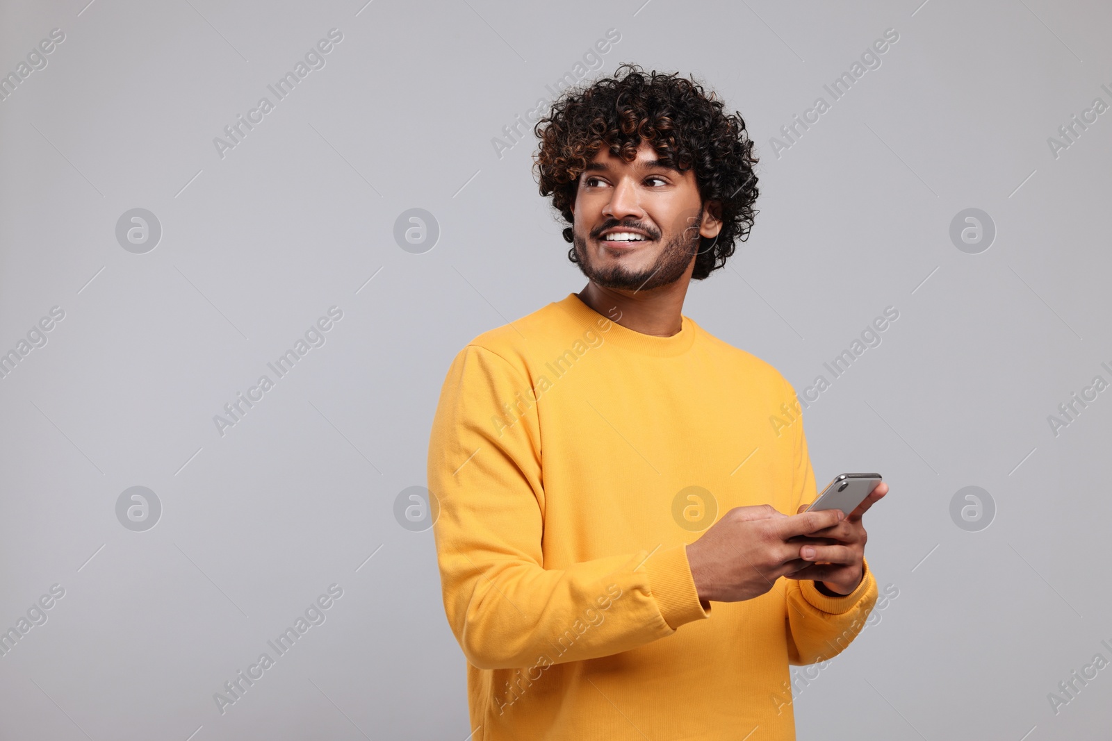 Photo of Handsome smiling man using smartphone on light grey background, space for text