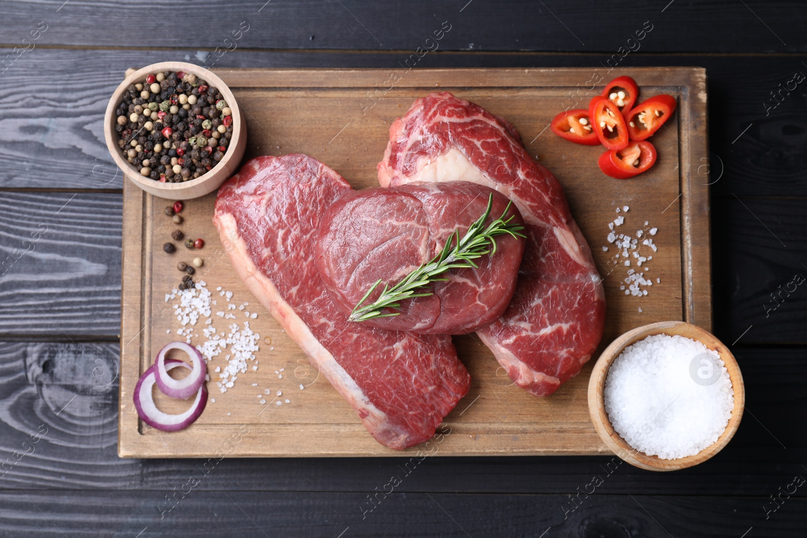 Photo of Pieces of raw beef meat and spices on black wooden table, top view