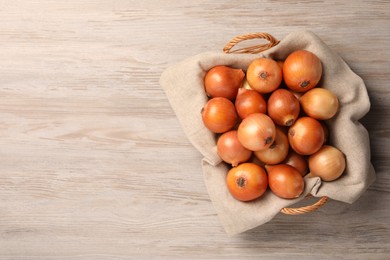 Photo of Wicker basket with many ripe onions on wooden table, top view. Space for text