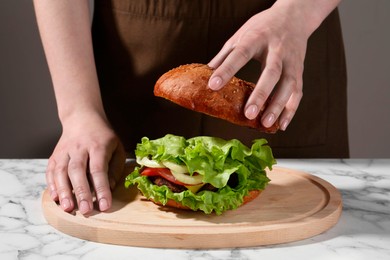 Photo of Woman making delicious vegetarian burger at white marble table, closeup