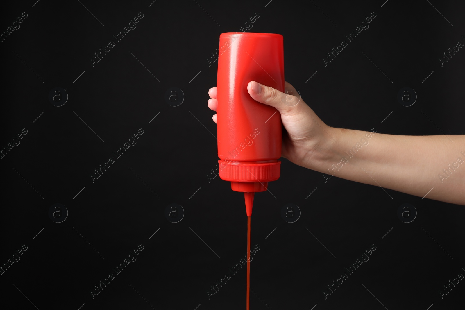 Photo of Woman pouring tasty ketchup from bottle on black background, closeup. Space for text