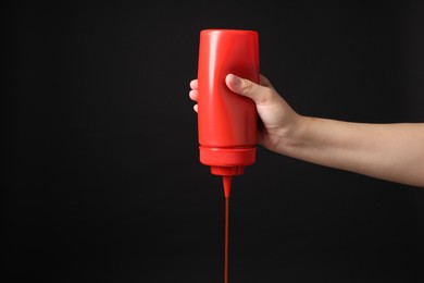 Photo of Woman pouring tasty ketchup from bottle on black background, closeup. Space for text