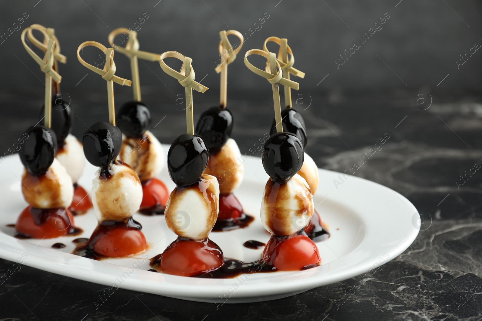 Photo of Tasty canapes with black olives, mozzarella and cherry tomatoes on dark textured table, closeup