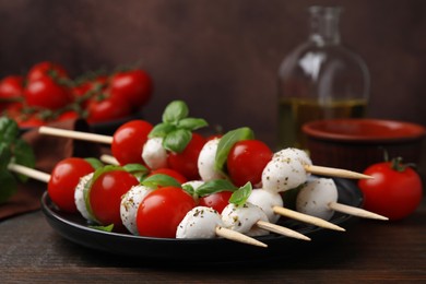 Photo of Delicious Caprese skewers with tomatoes, mozzarella balls, basil and spices on wooden table, closeup