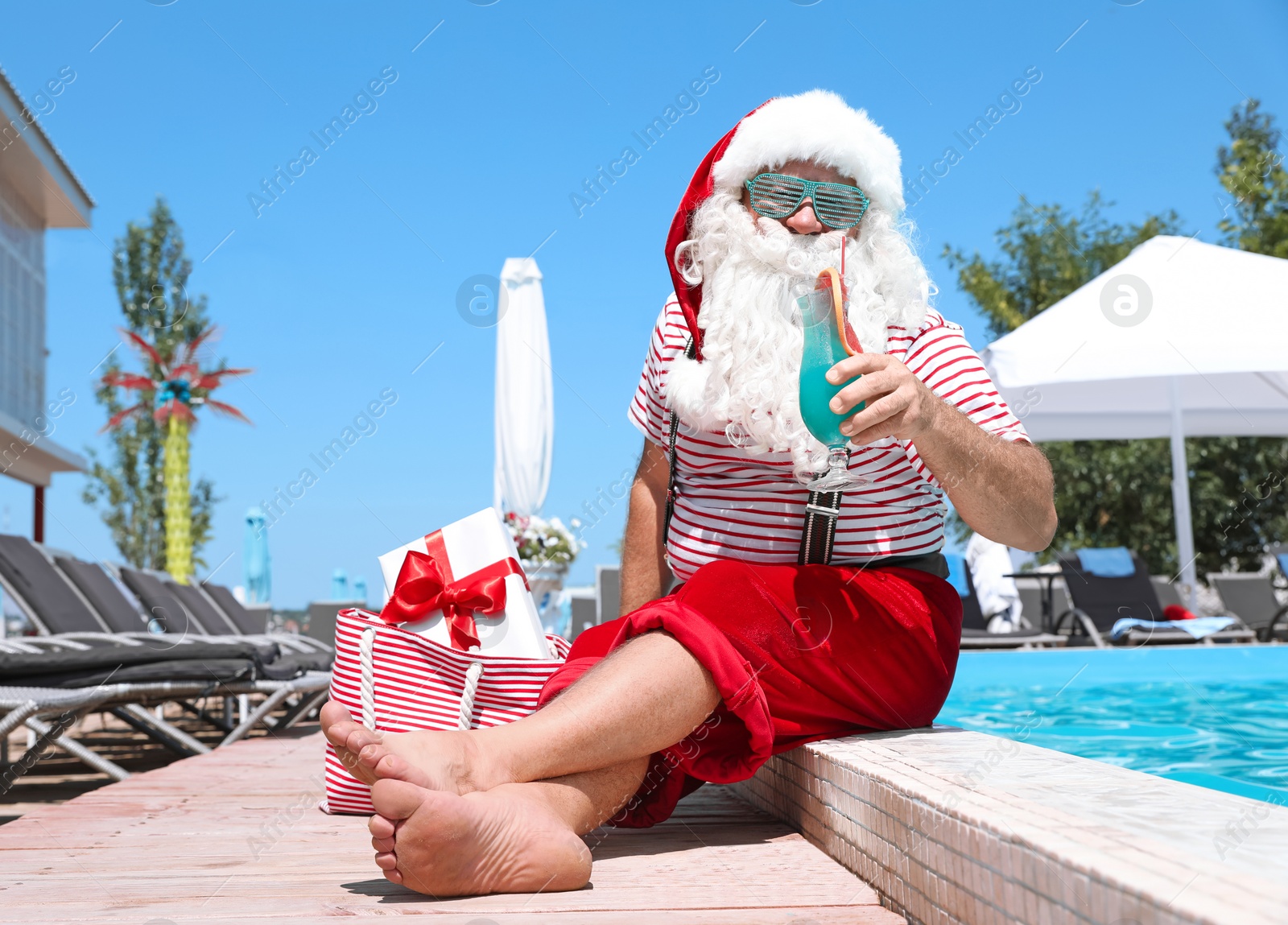 Photo of Authentic Santa Claus with cocktail and gift in bag near pool at resort