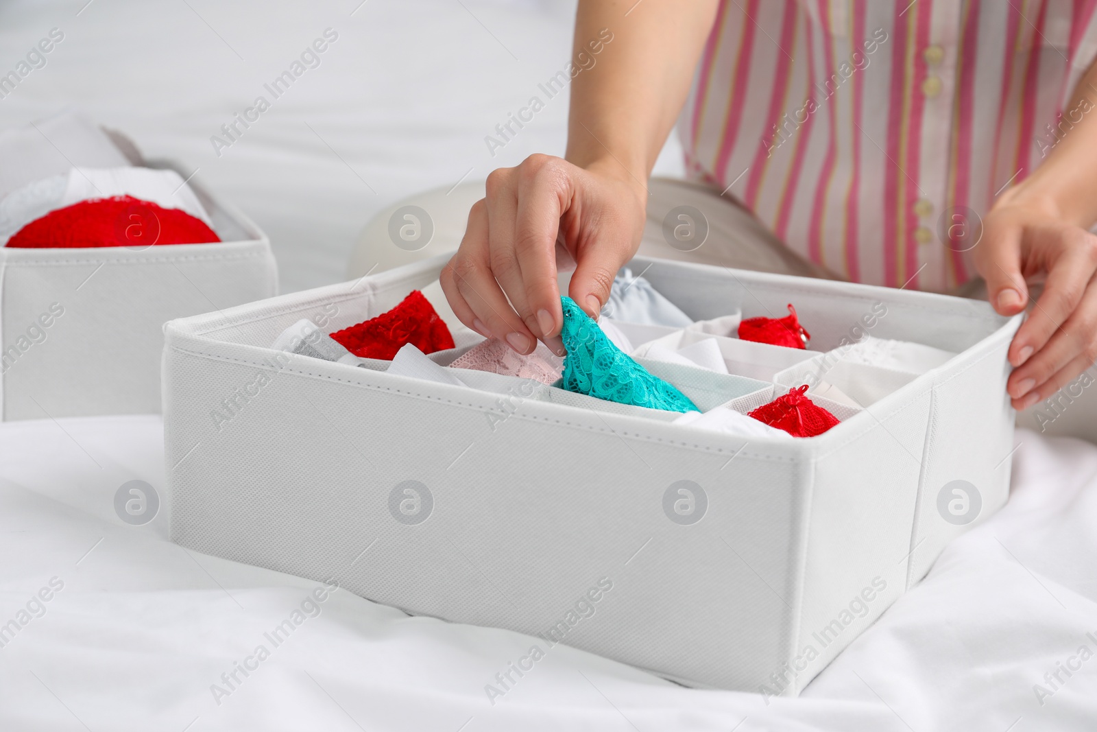 Photo of Woman putting underwear into organizer on bed, closeup