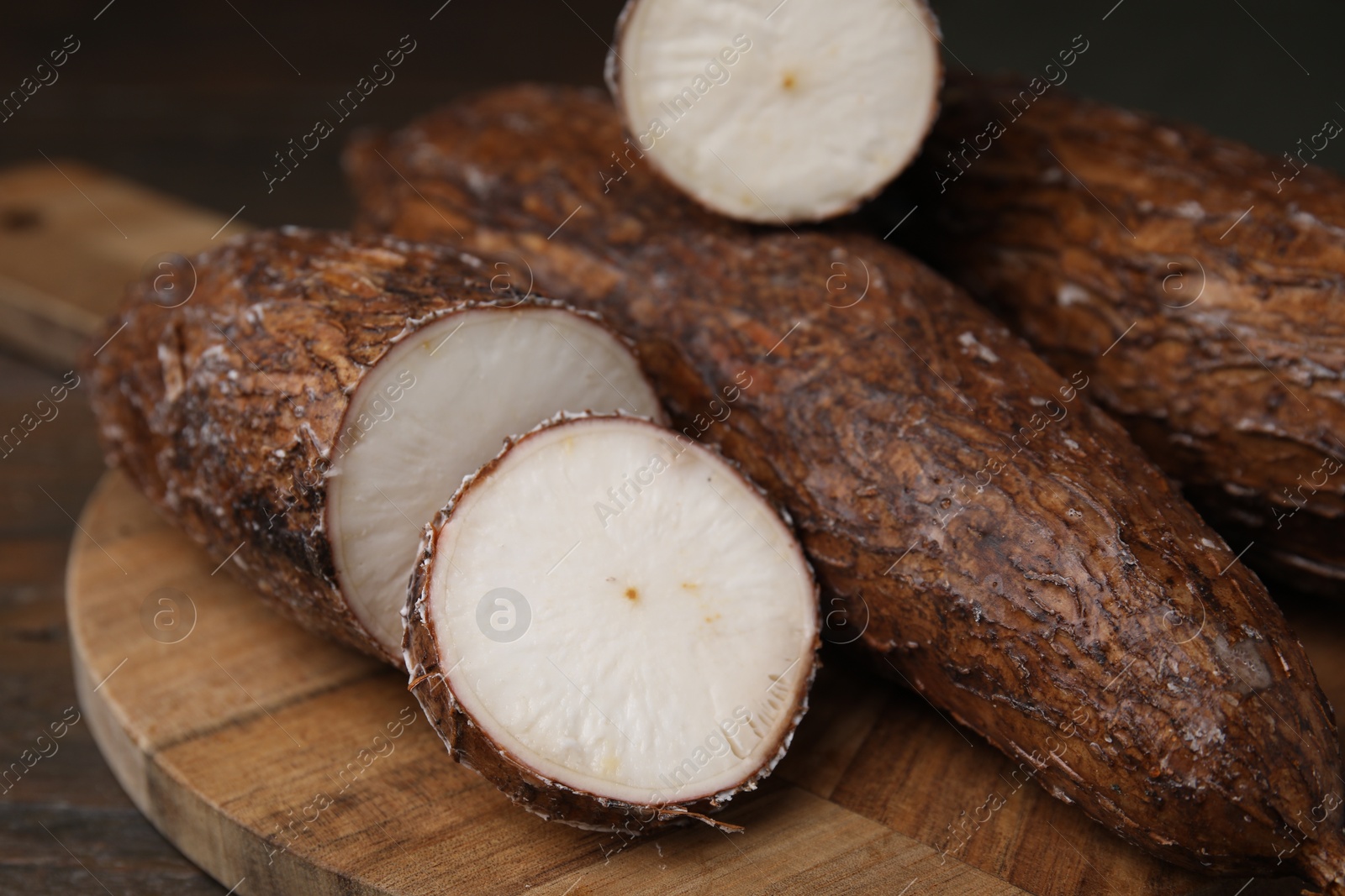 Photo of Whole and cut cassava roots on wooden table, closeup