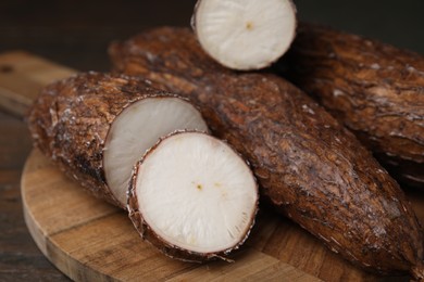 Photo of Whole and cut cassava roots on wooden table, closeup