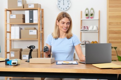 Photo of Seller with scanner reading parcel barcode at table in office. Online store