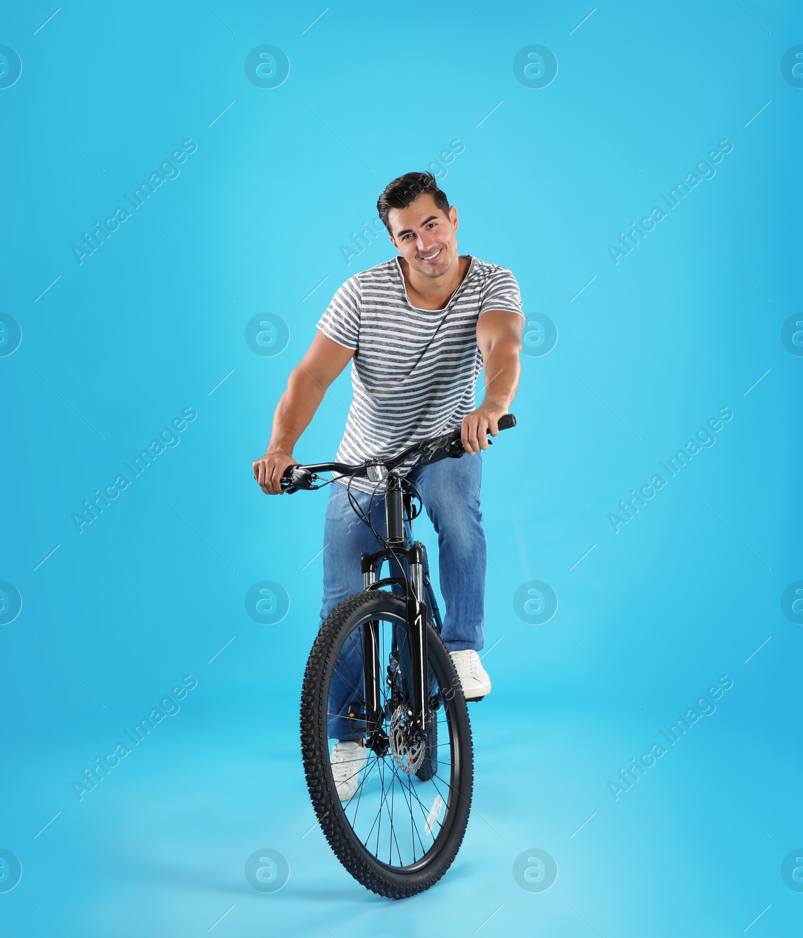 Photo of Handsome young man with modern bicycle on light blue background