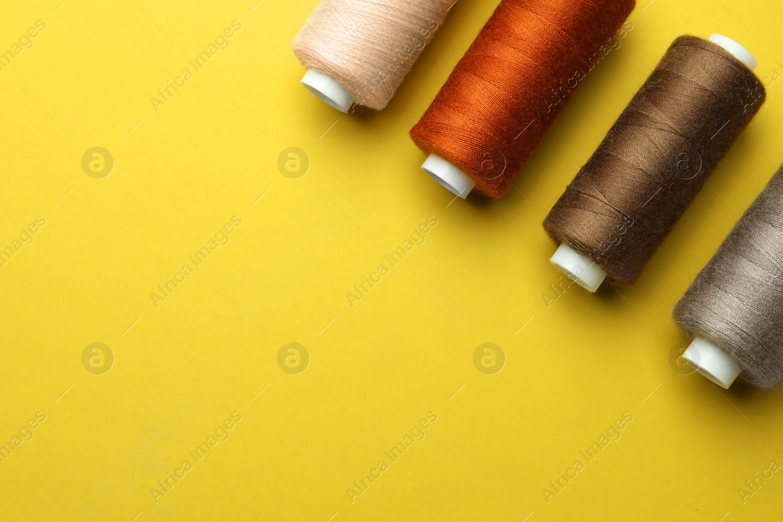 Photo of Different colorful sewing threads on yellow background, flat lay. Space for text