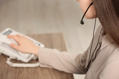 Photo of Hotline operator with headset and stationary phone working in office, closeup. Space for text