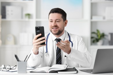 Photo of Doctor having online consultation via smartphone at table in clinic