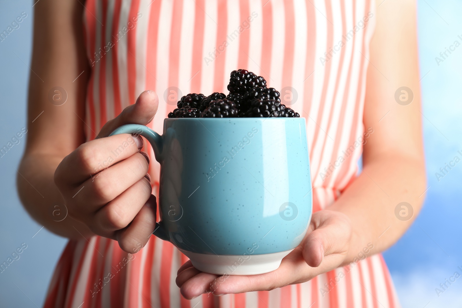 Photo of Woman holding mug of fresh blackberry against color background, closeup