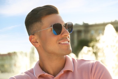 Photo of Handsome man wearing stylish sunglasses on city street, closeup