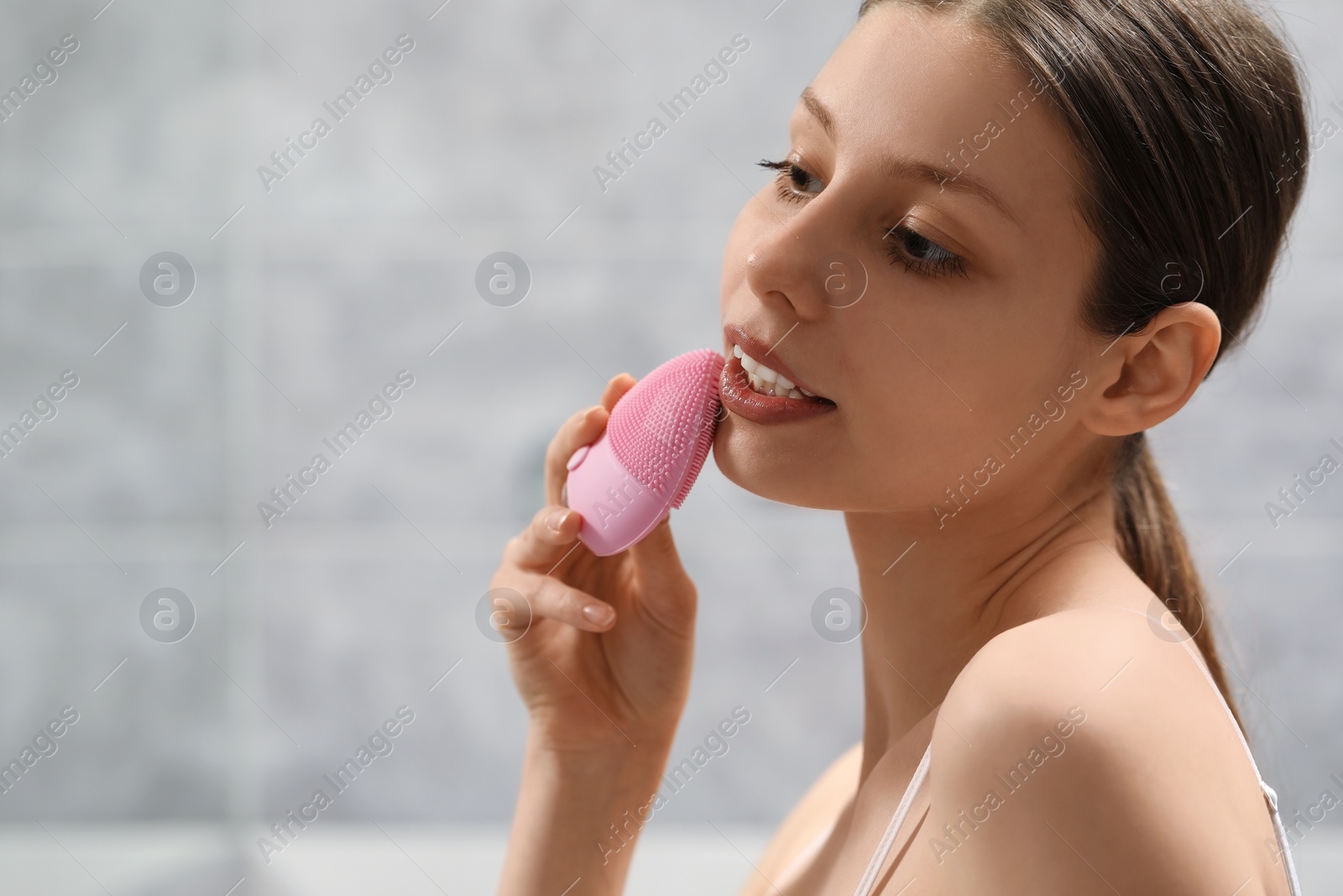 Photo of Washing face. Young woman with cleansing brush indoors, space for text