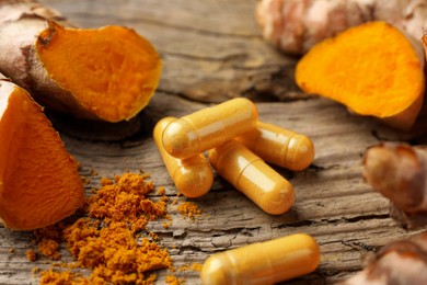 Photo of Aromatic turmeric powder, raw roots and pills on wooden surface, closeup