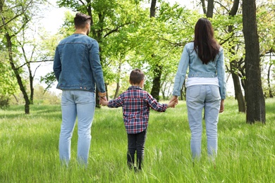 Photo of Little child holding hands with his parents in park. Family time