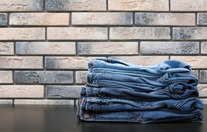 Photo of Stack of stylish jeans on table against brick wall