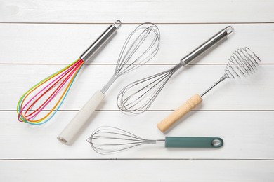 Different whisks on white wooden table, flat lay