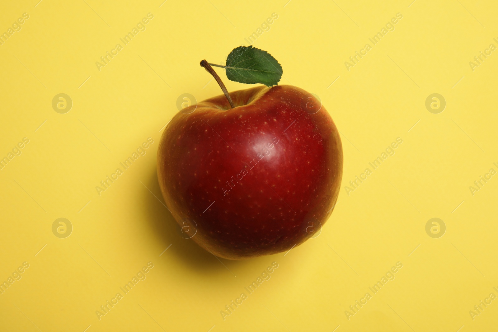 Photo of Ripe juicy red apple with leaf on yellow background, top view