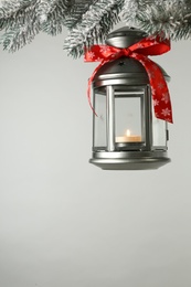 Photo of Christmas lantern with candle hanging on snowy fir tree branch against light background. Space for text