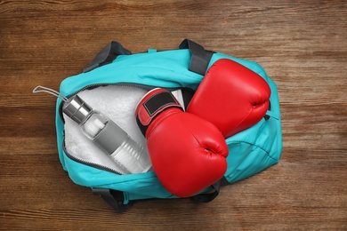 Photo of Sports bag with gym equipment on wooden background, top view