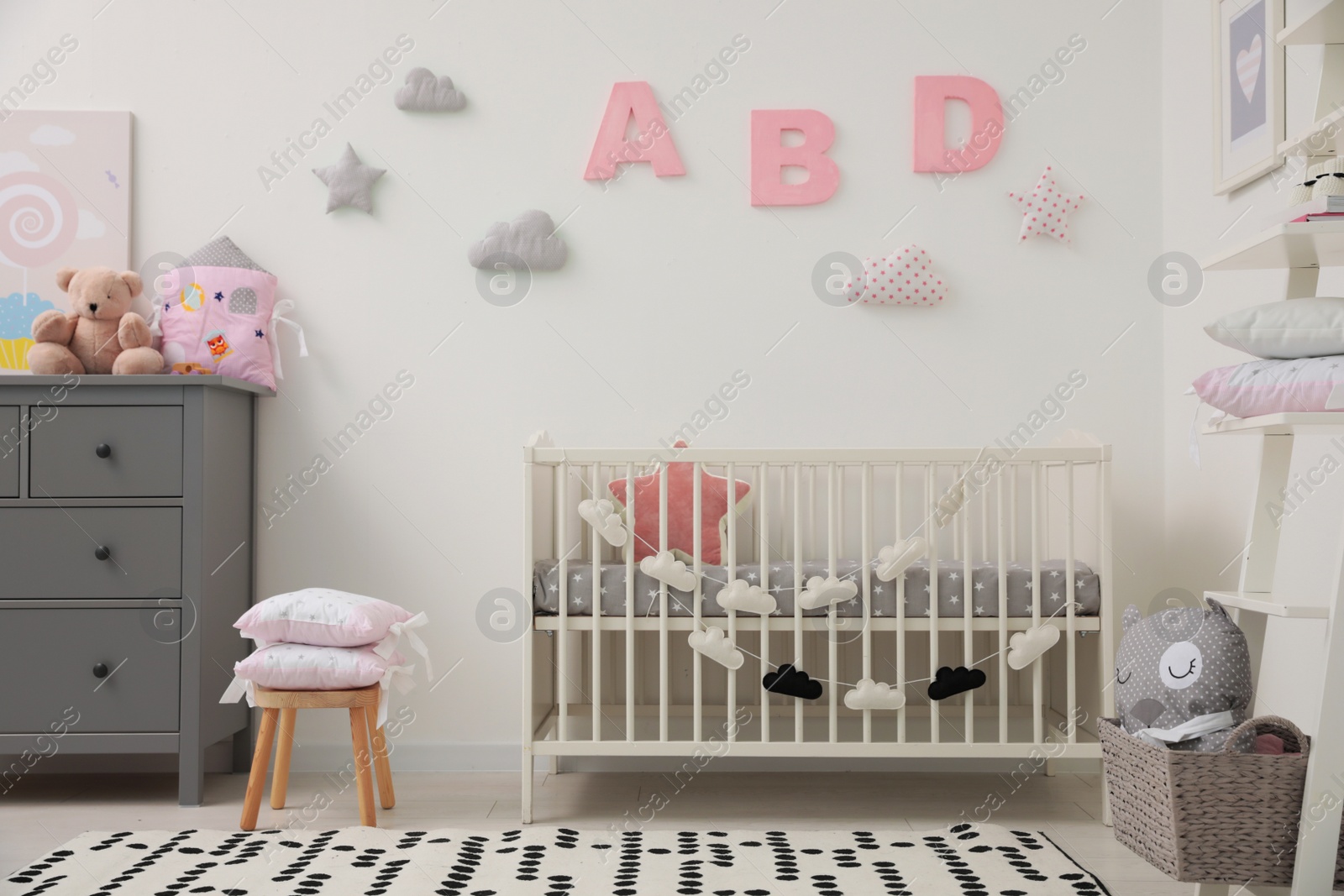 Photo of Cute baby room interior with crib and chest of drawers near white wall