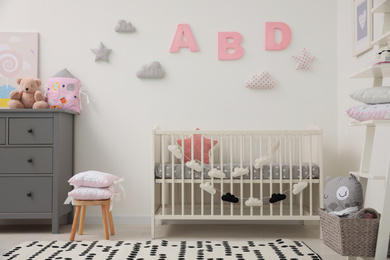 Cute baby room interior with crib and chest of drawers near white wall