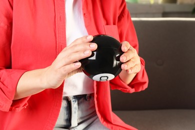 Photo of Woman holding magic eight ball indoors, closeup. Space for text