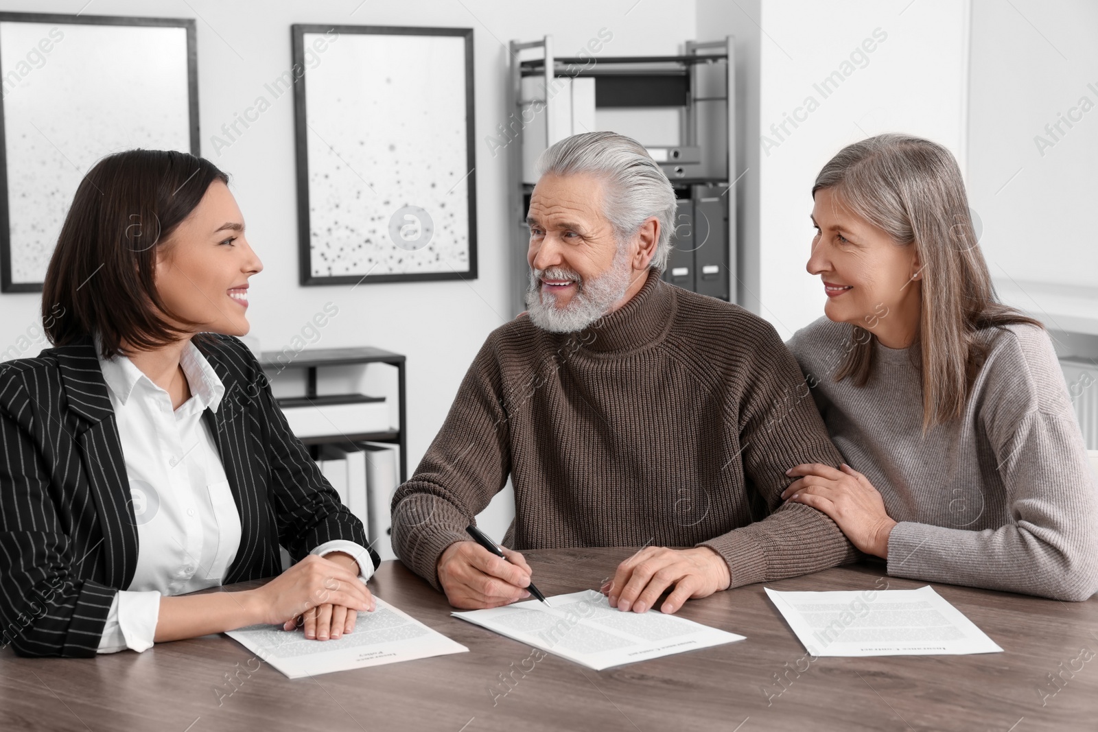 Photo of Elderly couple consulting insurance agent about pension plan at wooden table indoors