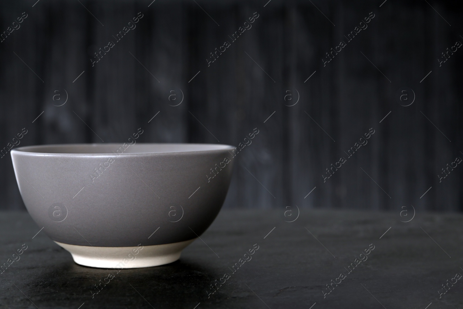 Photo of Stylish empty ceramic bowl on black table, space for text. Cooking utensil