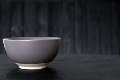 Stylish empty ceramic bowl on black table, space for text. Cooking utensil