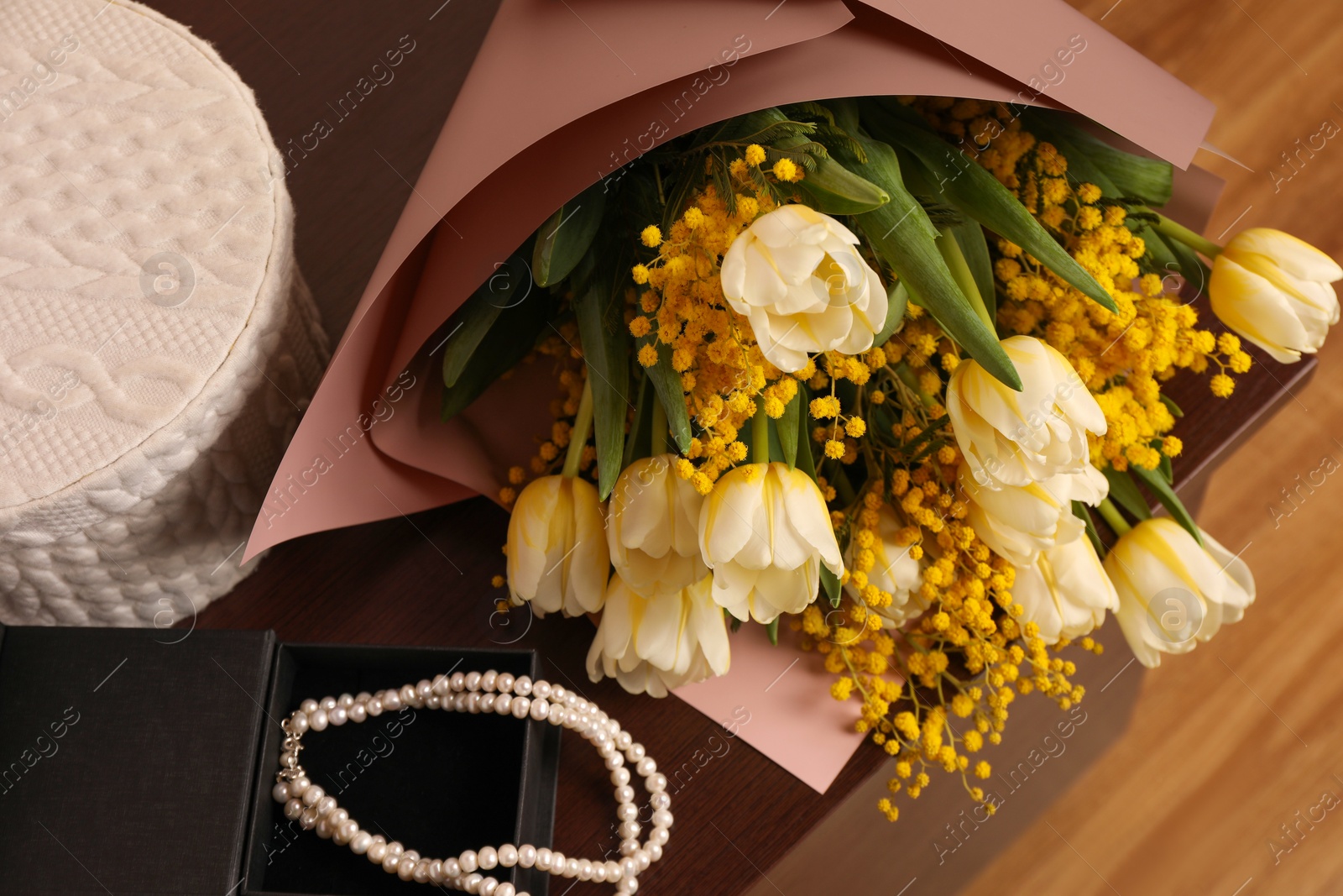 Photo of Bouquet with beautiful spring flowers and necklace on wooden chest of drawers, above view
