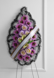 Photo of Funeral wreath of plastic flowers with ribbon near white wall
