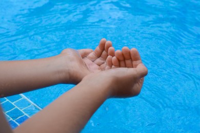 Photo of Girl holding water in hands above pool, closeup