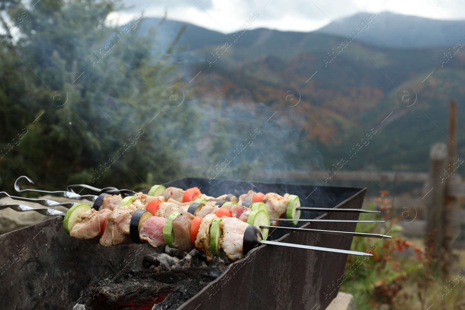 Photo of Cooking meat and vegetables on brazier against mountain landscape