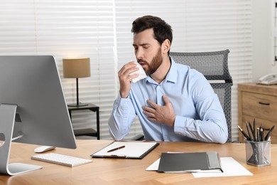 Photo of Sick man with tissue coughing at workplace in office