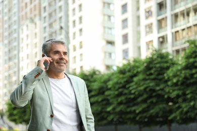 Photo of Handsome mature man talking on phone in city center. Space for text