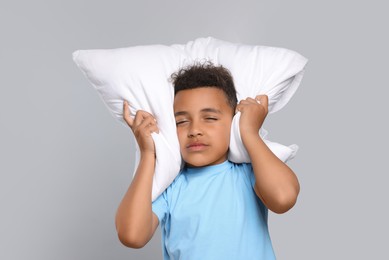 Boy covering his ears with pillow on grey background. Insomnia problem