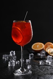 Glass of tasty Aperol spritz cocktail with orange slices and ice cubes on table against black background