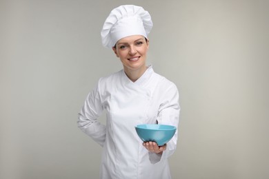 Happy chef in uniform holding bowl on grey background