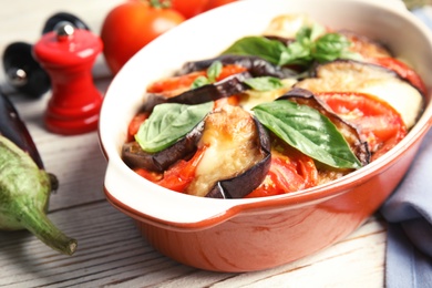 Photo of Baked eggplant with tomatoes, cheese and basil in dishware on table, closeup