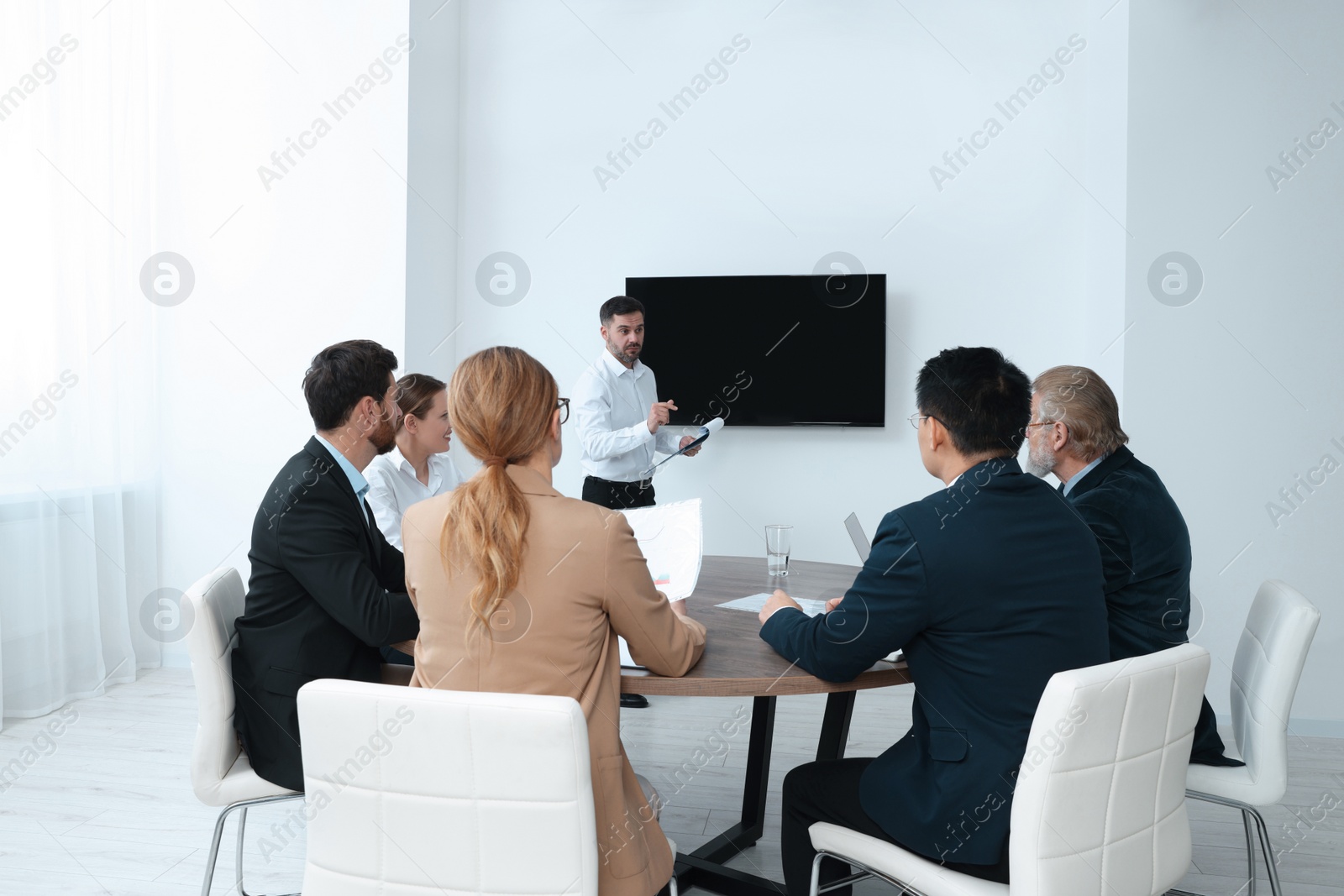 Photo of Business conference. Group of people listening to speaker report near tv screen in meeting room